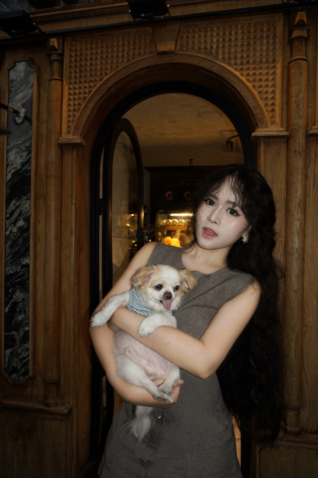 Clara holding her dog beneath an ornate wooden arch